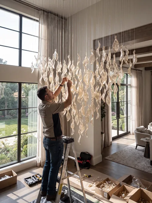 Technician installing a crystal chandelier in a luxury interior